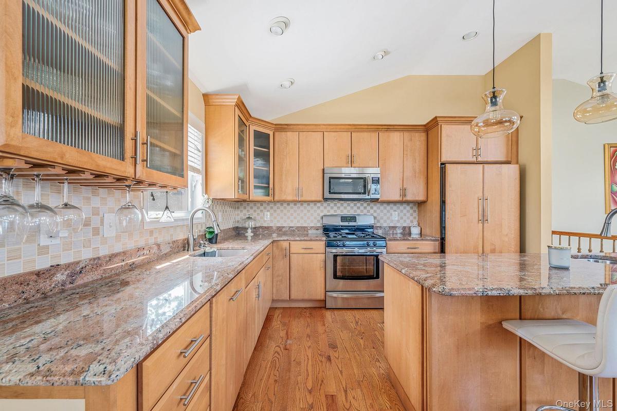 Kitchen with decorative backsplash, a breakfast bar, stainless steel appliances, light wood-style floors, and vaulted ceiling