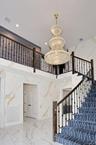 Staircase with stone wall, marble tiled floors, a high ceiling, a chandelier, and recessed lighting