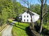 View of side of home with asphalt driveway, a lawn, and a wooded view