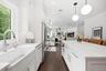 Gourmet kitchen featuring a farmhouse sink with built in food disposal, and a spacious island with Carrera gold Silestone countertops and pendant ligh