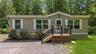 Exterior featuring tan siding, white window shutters, and a front porch with black railing