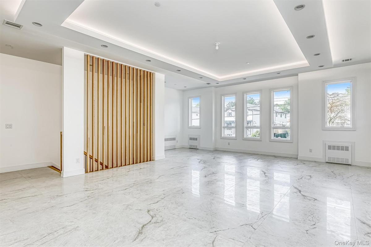 Empty room with a tray ceiling, light marble finish flooring, and radiator heating unit