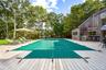 View of swimming pool featuring view of wooded area, a covered pool, a wooden deck, and grilling area