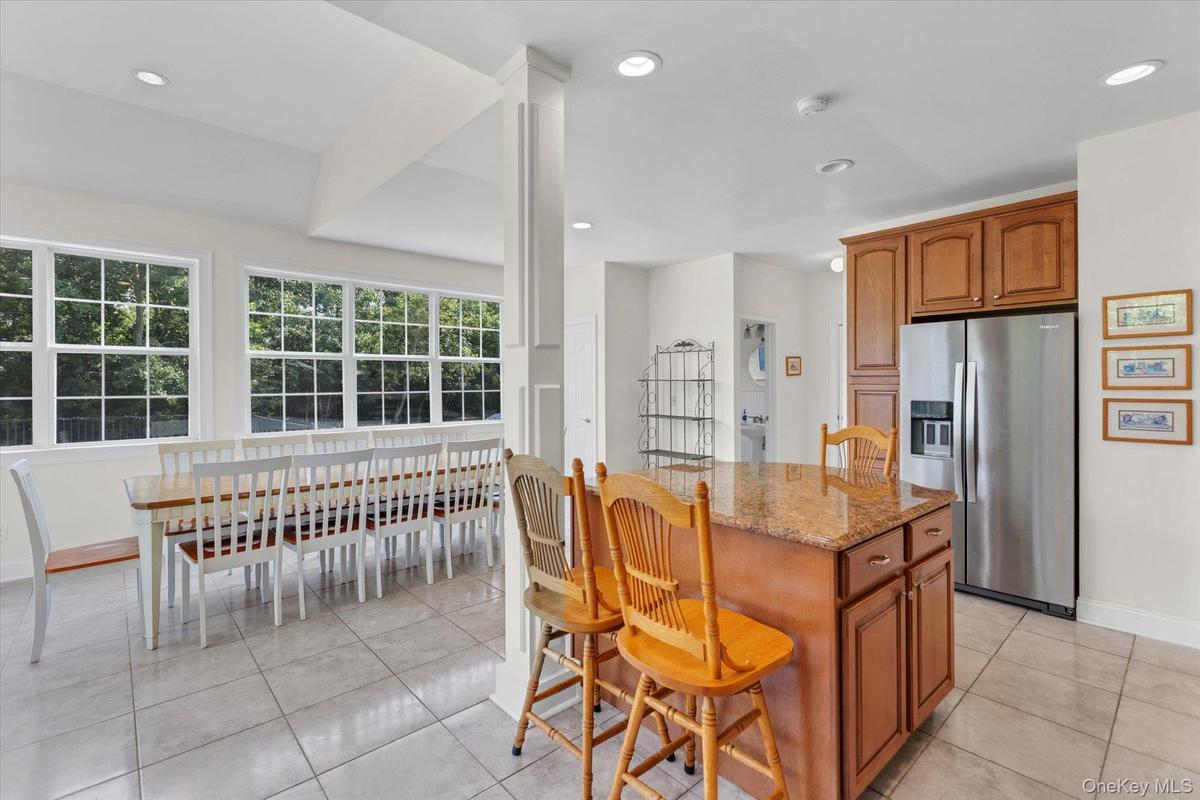 Kitchen with wood cabinetry, stainless steel refrigerator, and a granite-topped island