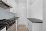 Galley kitchen featuring white cabinetry, dark countertops, a gas range with stainless steel oven, an undermount sink, and a light blue tiled backspla