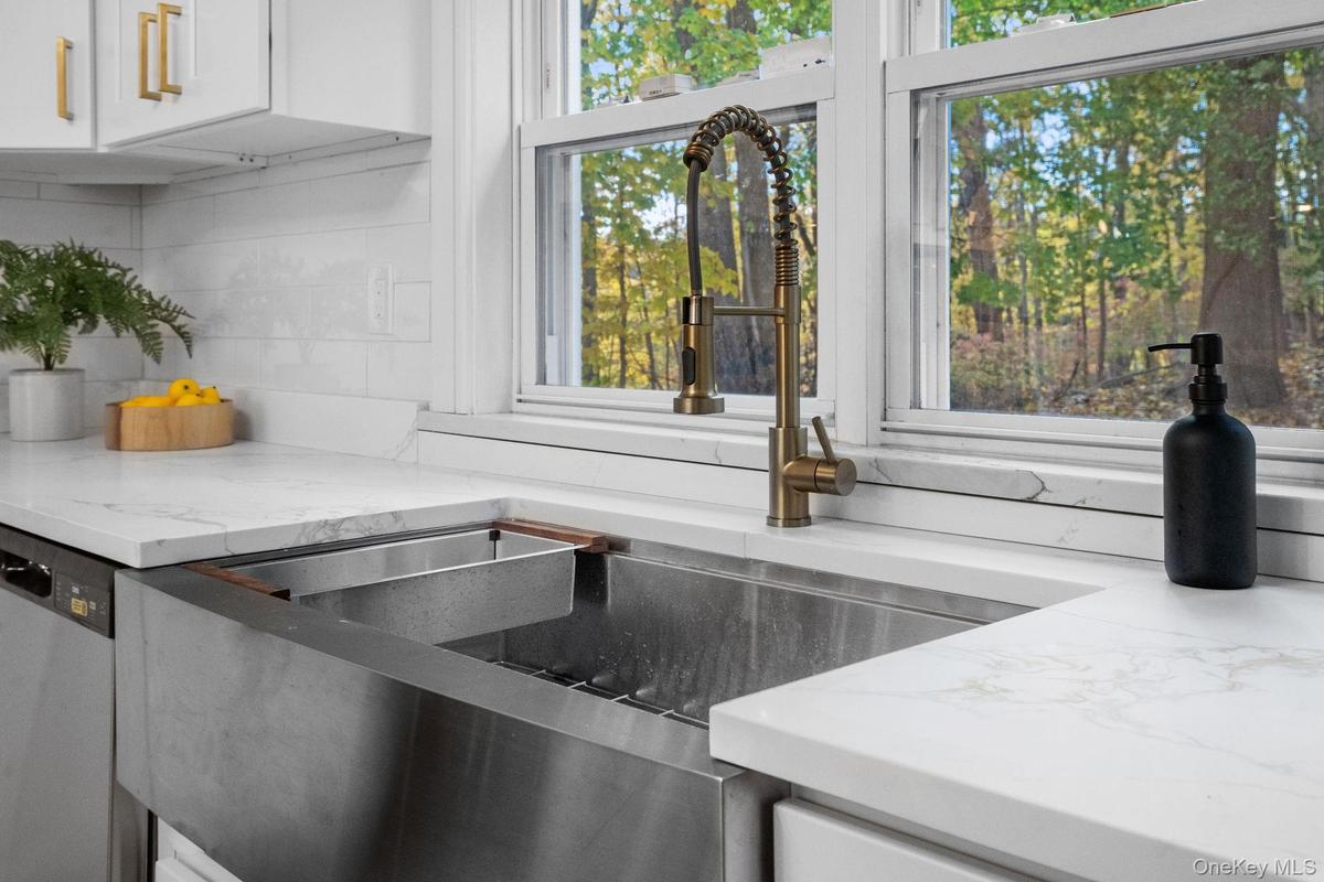 Stylish farmhouse sink with brass faucet and quartz countertops overlooks the private backyard, adding beauty to everyday routines.