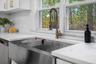 Stylish farmhouse sink with brass faucet and quartz countertops overlooks the private backyard, adding beauty to everyday routines.