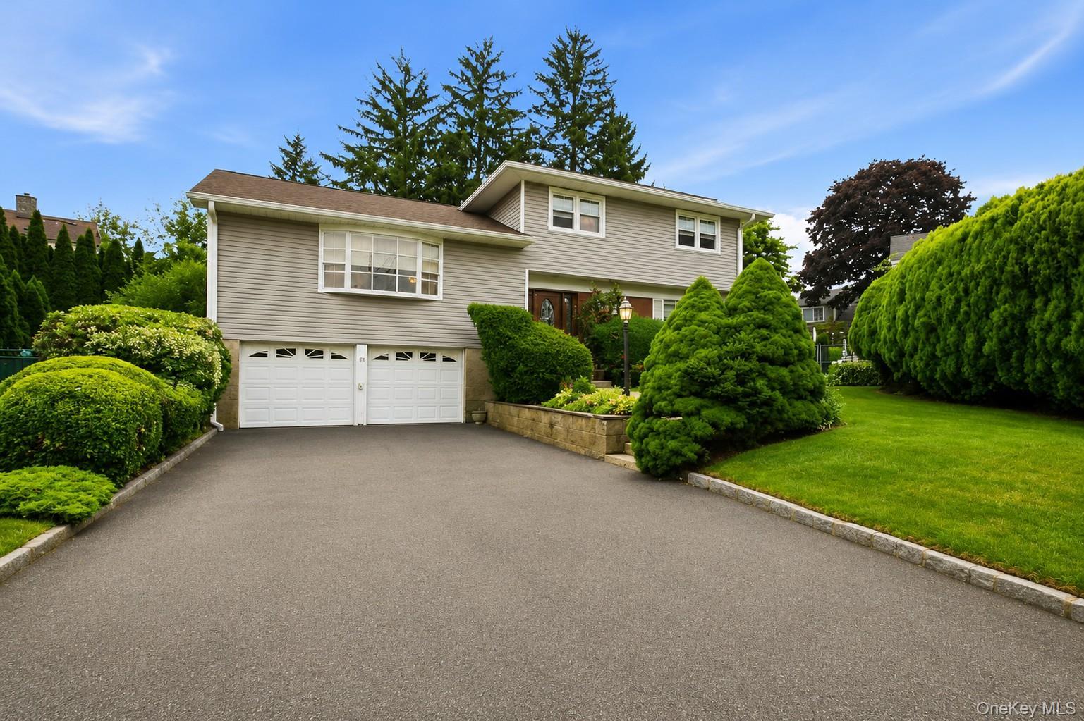 Split-level residence featuring light-colored siding and a two-car garage with white paneled doors