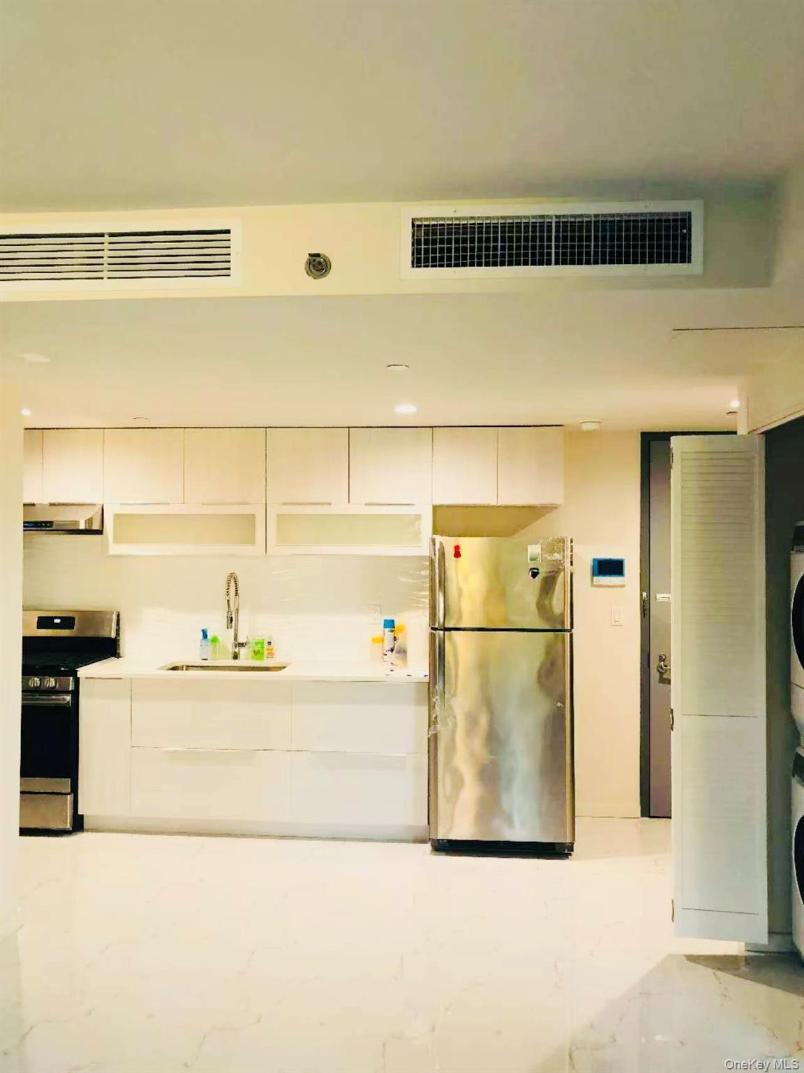 Kitchen with stainless steel appliances, white cabinetry, modern cabinets, exhaust hood, and stacked washer / drying machine