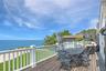 Wooden deck featuring outdoor dining space, a water view, and a lawn