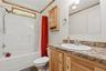 Bathroom featuring a white tub/shower combination with a transom window, a vanity with a built-in sink, a speckled countertop, and light wood cabinetr