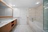 Bathroom featuring tile walls, double vanity, tiled bath, a wainscoted wall, and recessed lighting