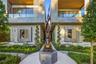 Close-up of paver entry walkway centered on large-scale bronze figurative sculpture on stone pedestal, flanked by spiral topiaries, reflecting pools,