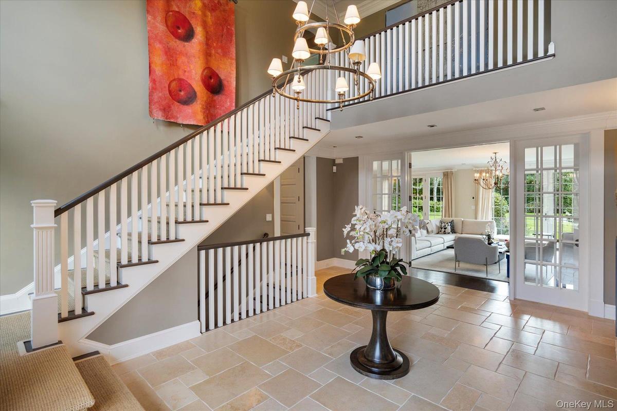 Stairs with a chandelier, a towering ceiling, crown molding, and stone tile flooring
