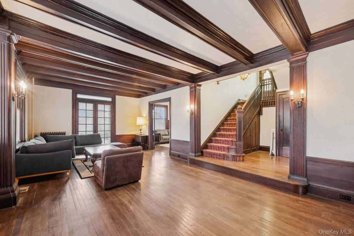 Living room featuring ornate columns, beamed ceiling, wainscoting, stairway, and wood-type flooring