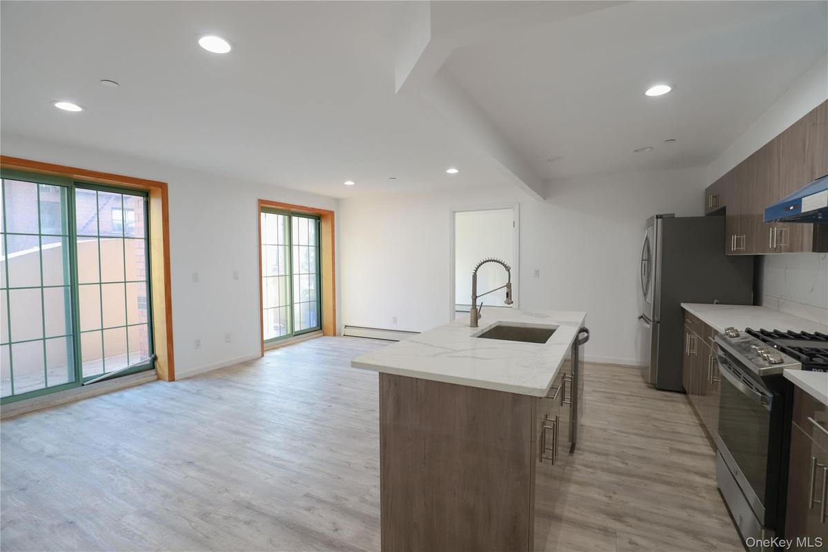 Kitchen featuring recessed lighting, light wood-type flooring, light stone countertops, an island with sink, and appliances with stainless steel finis