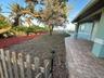 A charming Florida beachfront front yard with swaying trees, small rabbits, and birds. A paver path leads past oversized chairs to the front door.