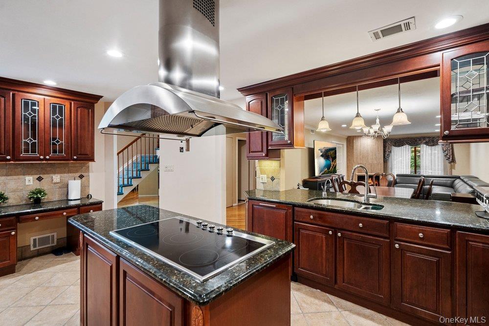 Gourmet kitchen featuring a central island with an electric cooktop, stainless steel range hood, stone countertops, and extensive wood cabinetry