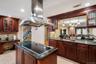 Gourmet kitchen featuring a central island with an electric cooktop, stainless steel range hood, stone countertops, and extensive wood cabinetry