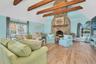 Staged Great room living area with high vaulted ceiling, a stone fireplace, light wood-type flooring, healthy amount of natural light, and beamed ceil