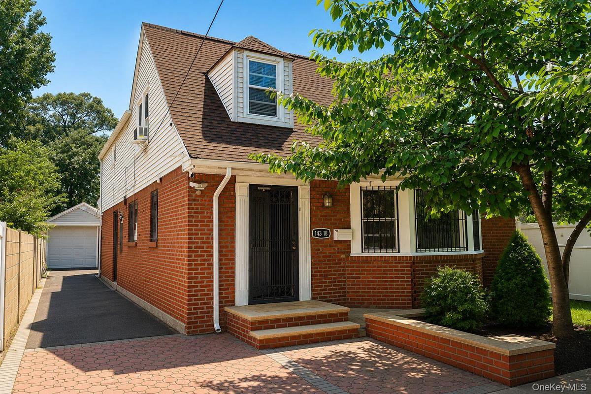 Brick facade home featuring a dormer window, paver driveway, and an attached single-car garage