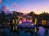 Aerial twilight view from canal showing two-story modern estate, private deep-water dock with large yacht, illuminated tropical landscaping, LED-lit p