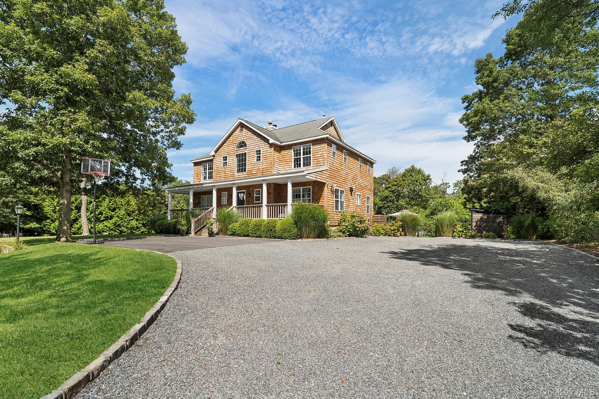 Shingle-style home with driveway, covered porch, and a front yard