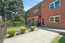 Brick facade exterior featuring a red entry door, a red striped awning, a concrete driveway, and a black wrought iron fence.