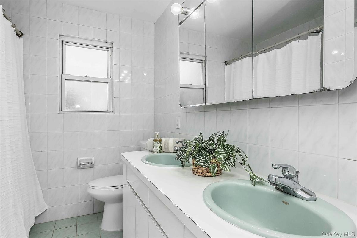 Bathroom featuring a dual basin vanity with integrated sinks, a wall-mounted medicine cabinet, white tiled walls,