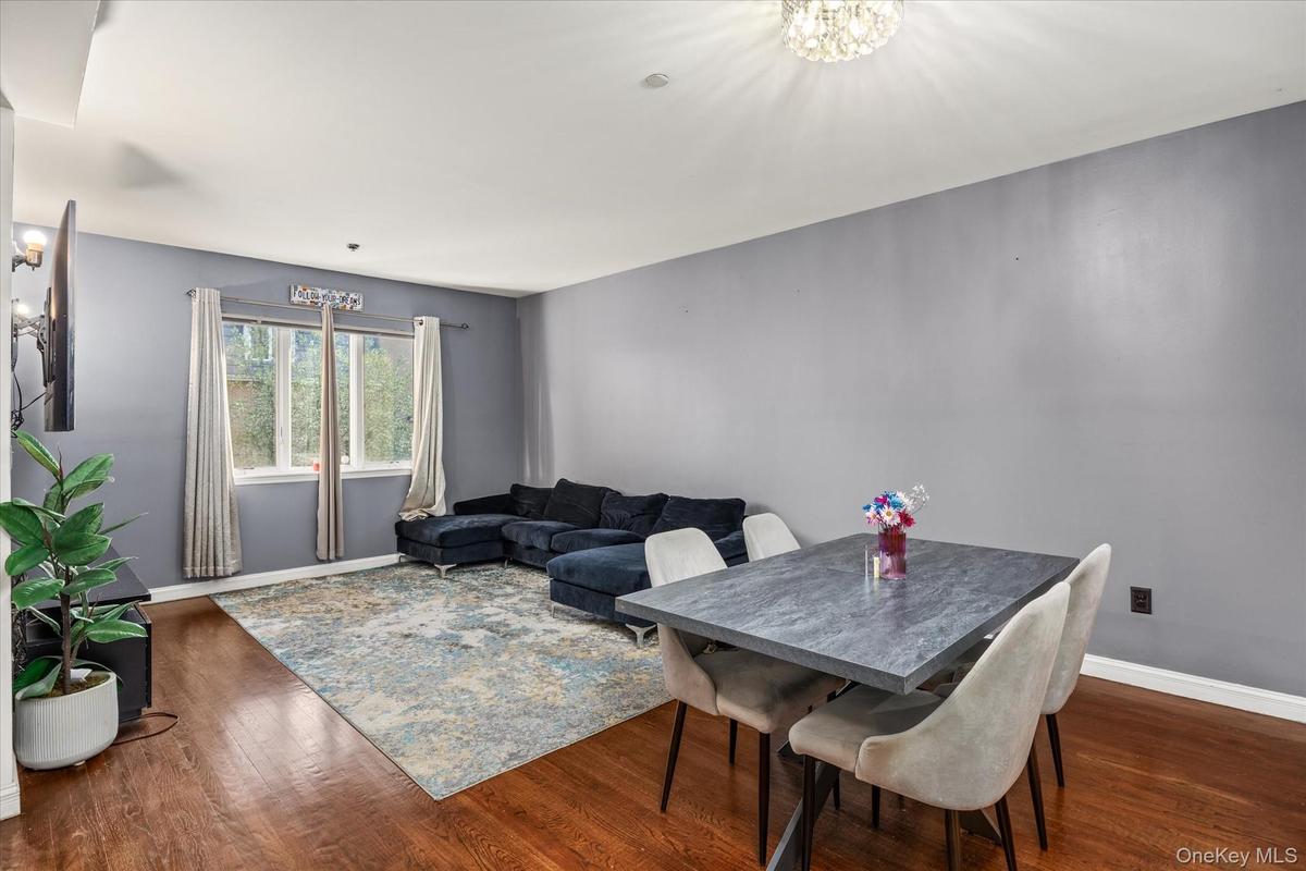 Open-concept living area featuring rich wood-finish flooring, a contemporary dining table, recessed lighting, and a prominent window providing natural