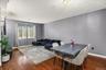Open-concept living area featuring rich wood-finish flooring, a contemporary dining table, recessed lighting, and a prominent window providing natural