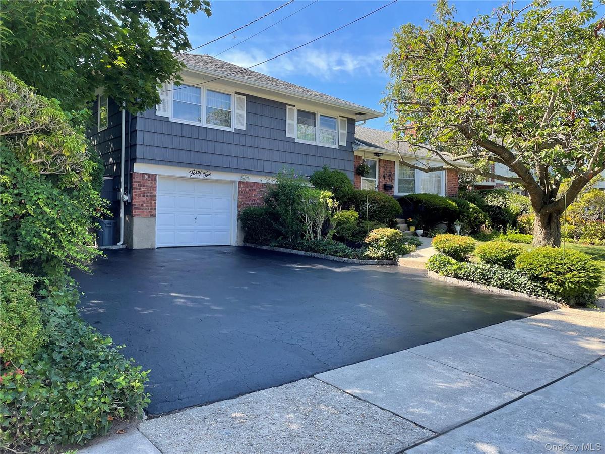 Split-level residence featuring a brick and shake exterior with white shutters, freshly sealed driveway and landscaped garden
