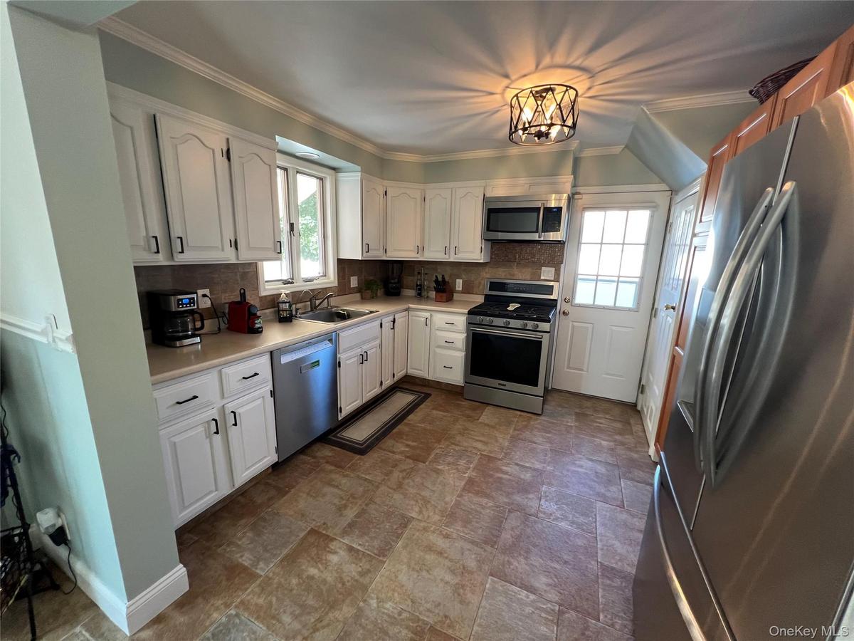 White cabinetry with black hardware, stainless steel appliances, stone-look tile flooring, and a decorative ceiling light fixture