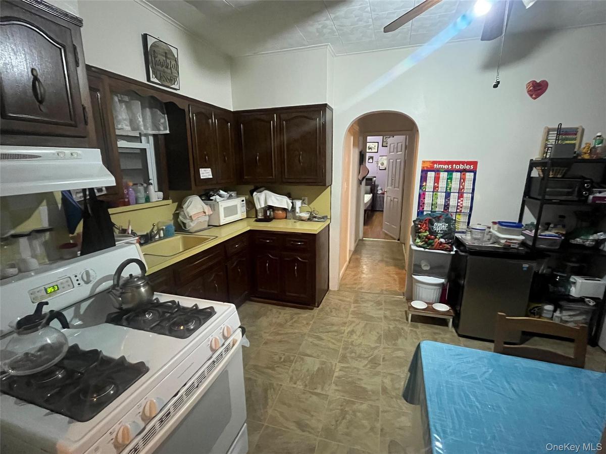 Kitchen with white appliances, dark brown cabinets, light countertops, a ceiling fan, and arched walkways