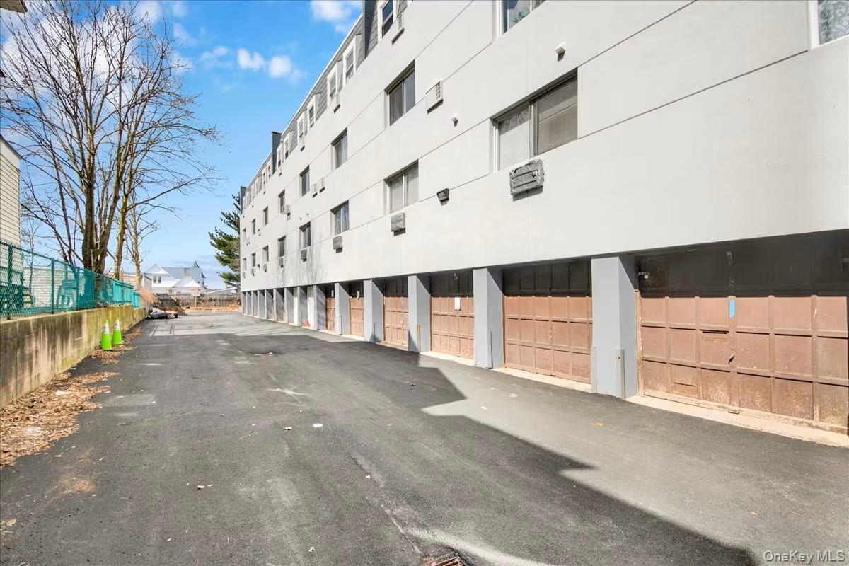 Multi-story building exterior with multiple ground-level garage doors, paved parking area, and a retaining wall