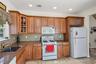 Kitchen featuring white appliances, brown cabinetry, dark stone countertops, tasteful backsplash, and recessed lighting