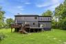 Rear exterior featuring a multi-level wood deck with black railings, a walk-out lower level, and a expansive grassy yard