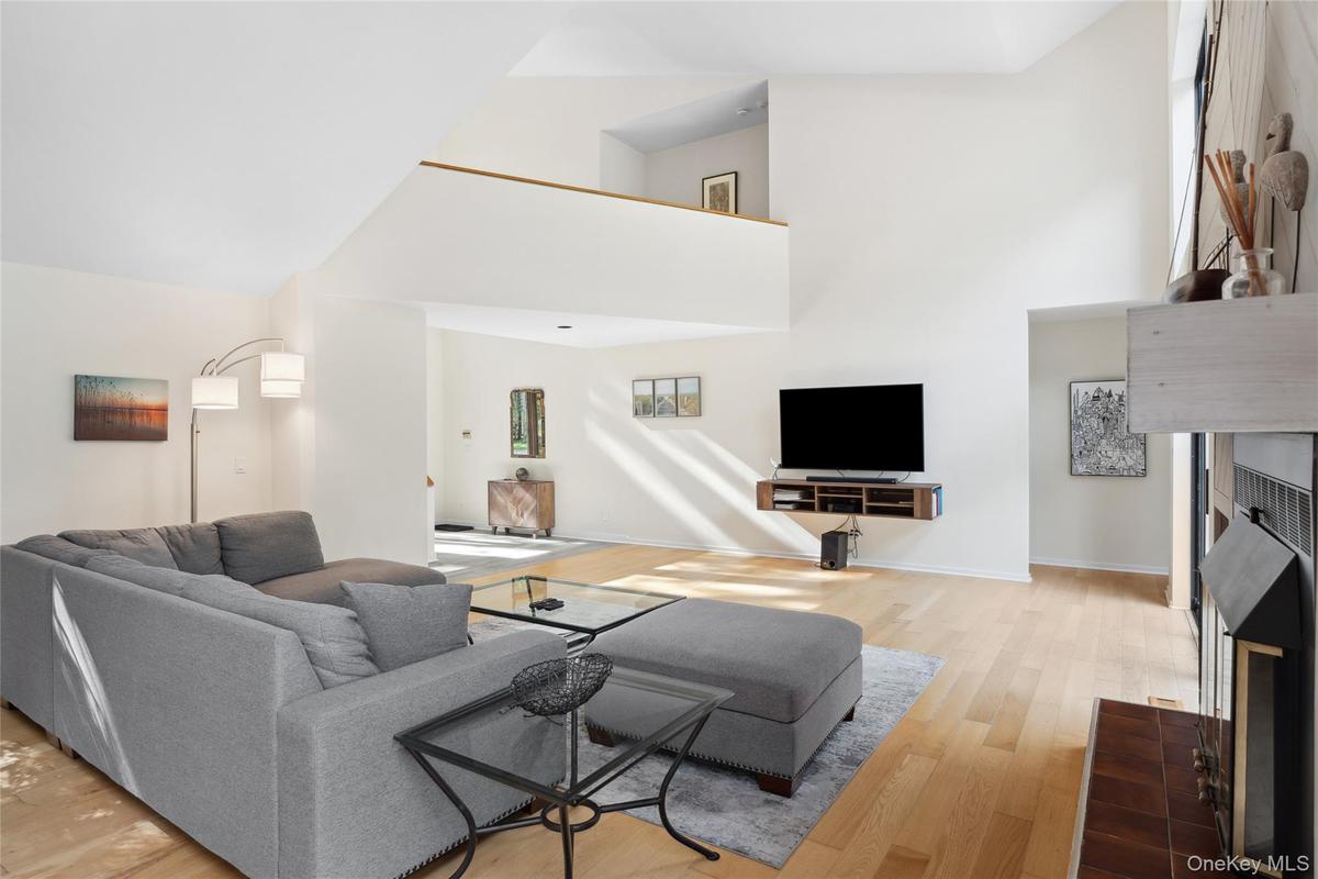 Living room featuring a tiled fireplace, light wood-style floors, and a towering ceiling