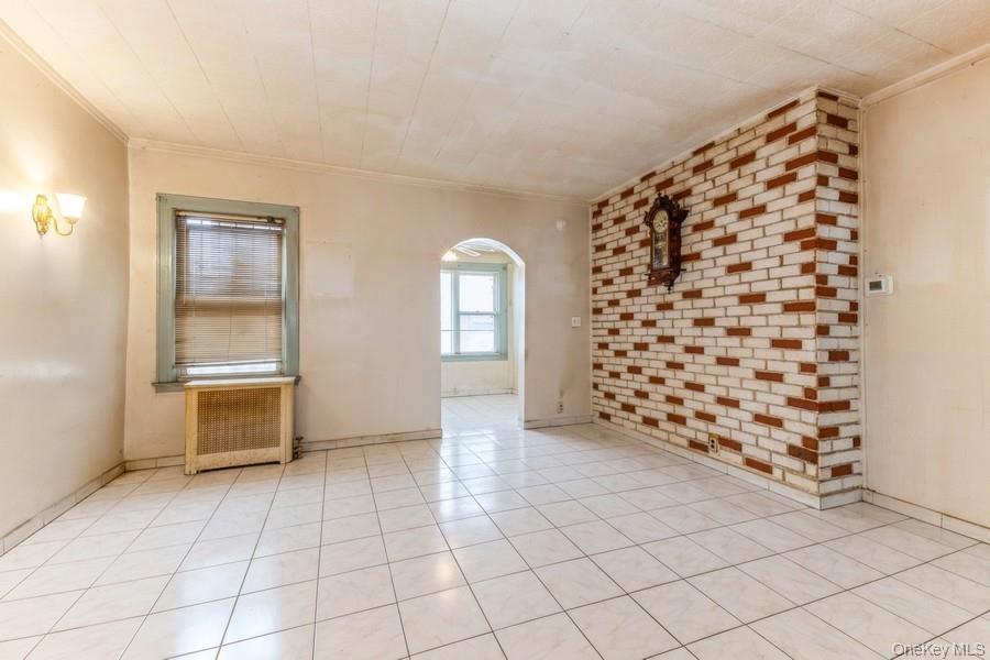 Spare room with arched walkways, radiator, light tile patterned flooring, brick wall, and ornamental molding