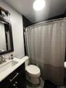 Bathroom featuring a dark subway tile shower surround, black vanity with gold-tone hardware, white countertop, and a brushed nickel faucet.Full Apt. #