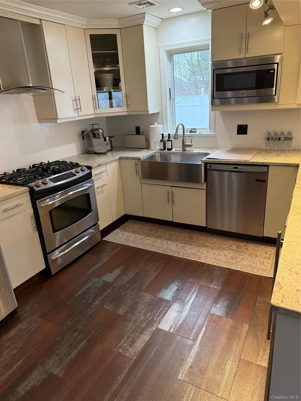 Kitchen with a sink, ventilation hood, dishwashing machine, range, and dark wood-style flooring