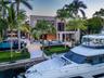 Low aerial dusk view from canal showing full waterfront rear elevation, private dock with large motor yacht, illuminated stepped terraces, glass-raile