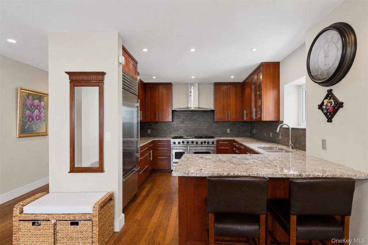 Kitchen featuring wood-finish flooring, custom wood cabinetry, stainless steel appliances, and stone countertops