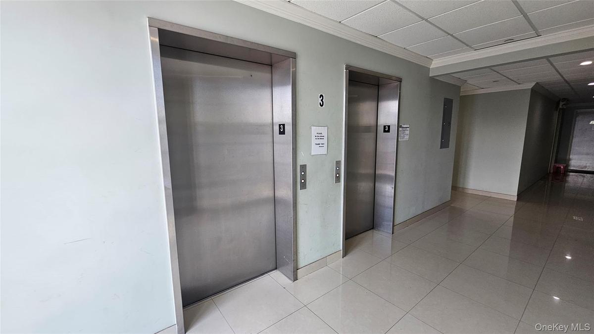 Corridor featuring elevator, tile patterned floors, crown molding, and a paneled ceiling