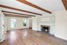 Living area featuring a stone fireplace with a decorative mantel, exposed wood ceiling beams, wood-finish flooring, and multiple windows