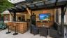 Outdoor entertainment area featuring a corrugated metal roof, wood shake bar with a stone countertop, built-in media console with television, exterior