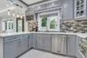 Contemporary kitchen featuring light gray cabinetry, white quartz countertops, undermount lighting, coutner seating