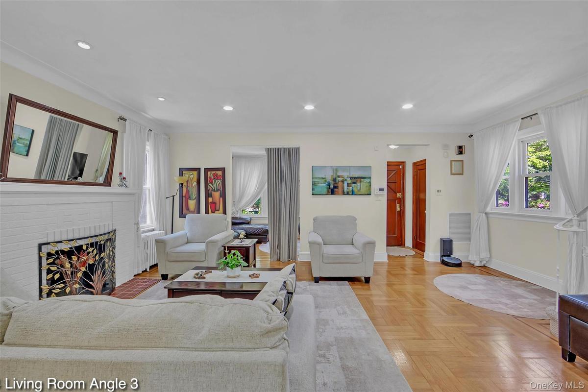 Spacious living area featuring parquet wood-finish flooring, recessed lighting, a white brick fireplace, and ample natural light from multiple windows
