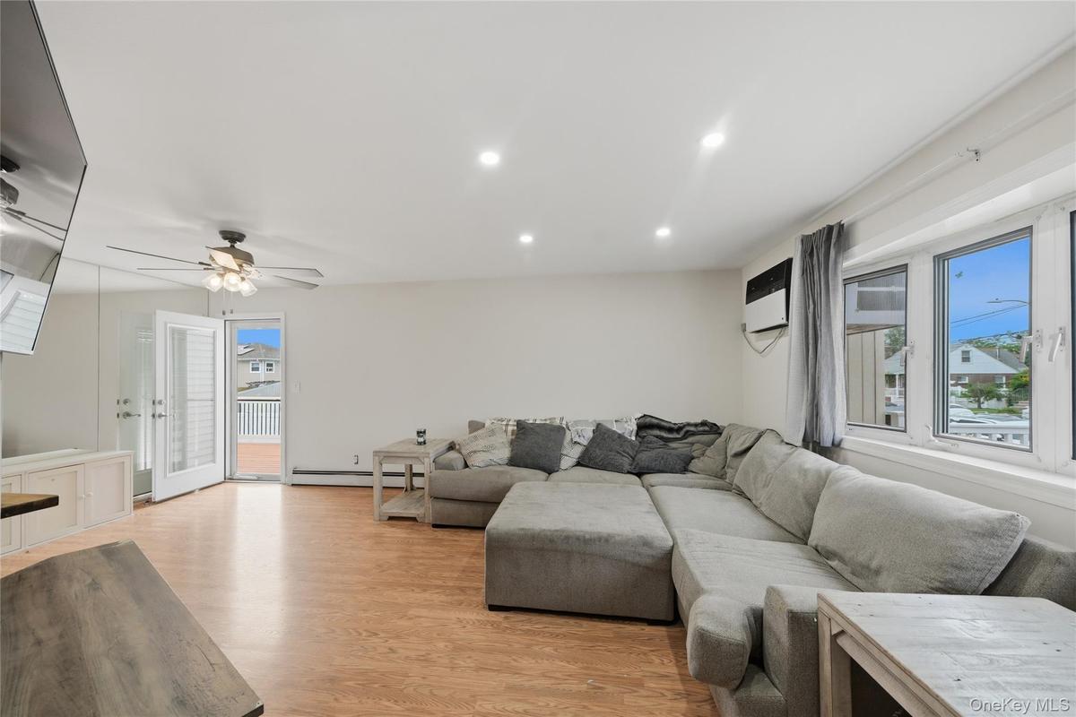 Bright open-concept living area featuring a sectional sofa arrangement, wood-finish flooring throughout, and abundant natural light from large multi-p