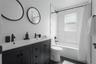 Full bathroom with double vanity, shower / bath combo with shower curtain, and dark tile patterned flooring